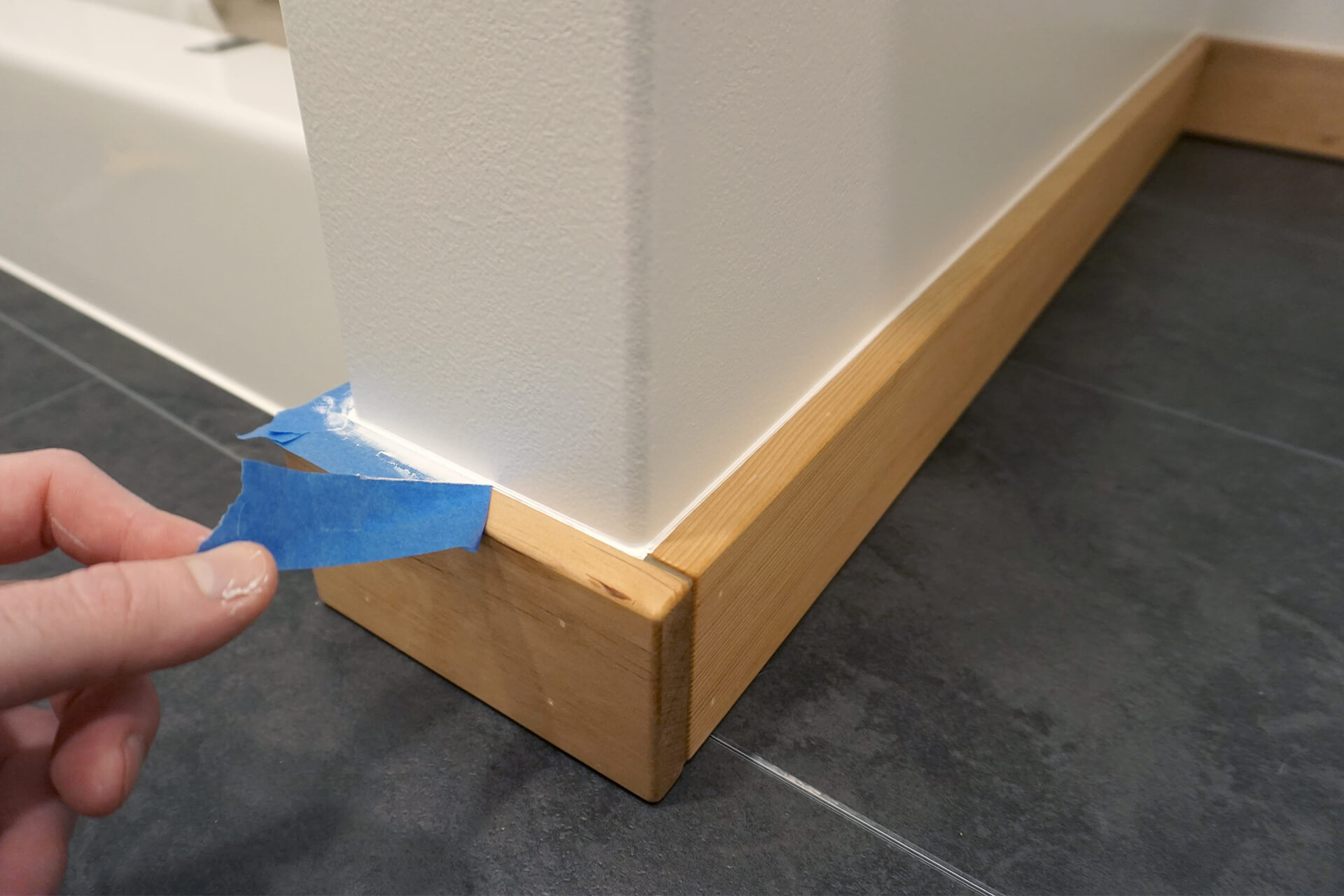 Peeling painter's tape off the newly installed and caulked bathroom baseboards.